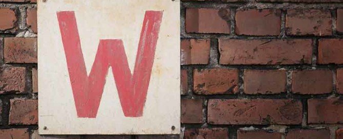 Cartello bianco, con all'interno una lettera W rossa, attaccato su un muro di mattoni